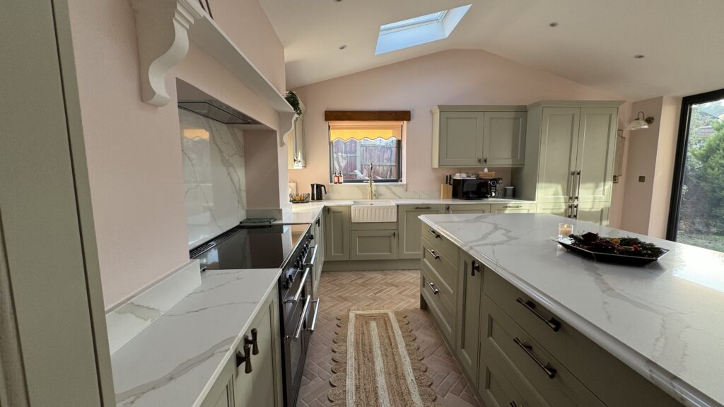 Open-plan kitchen with whole house refurbishment, featuring marble countertops, hidden appliances, and green cabinets inside a modern rear extension.